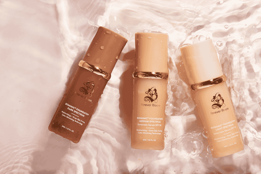 Forever Bloom's Biomimic® Foundation 4 in 1 in three shades, light, medium, and dark. The background is light pink and the foundations in a small base of water.