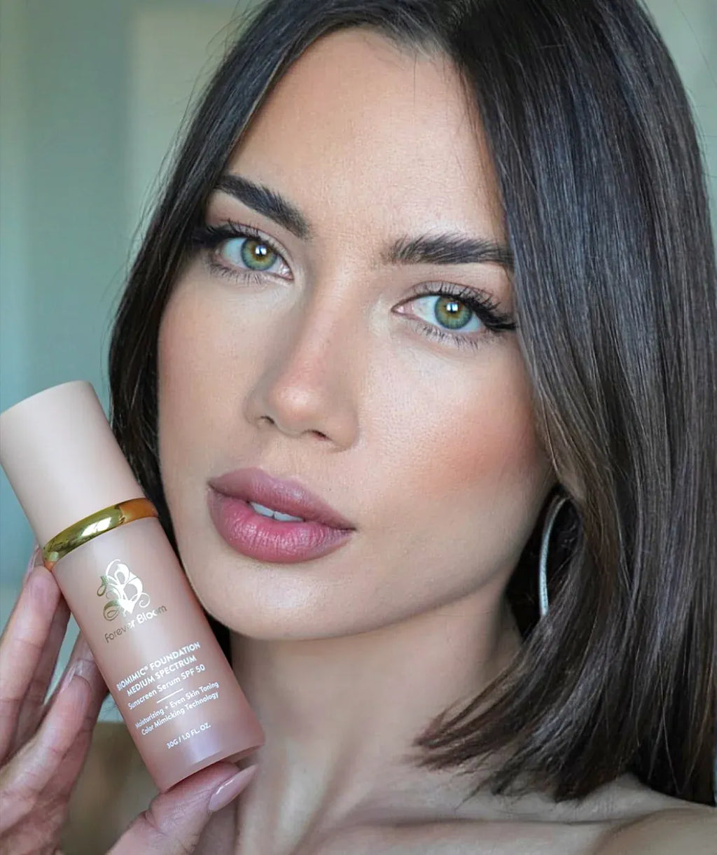 Woman holding a biomimc foundation medium product perfect match for her skin with a neutral background