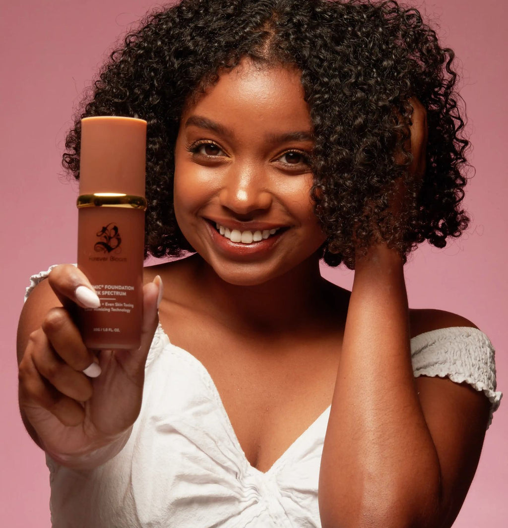 Woman with dark skin tone holding BioMimic color-changing foundation bottle
