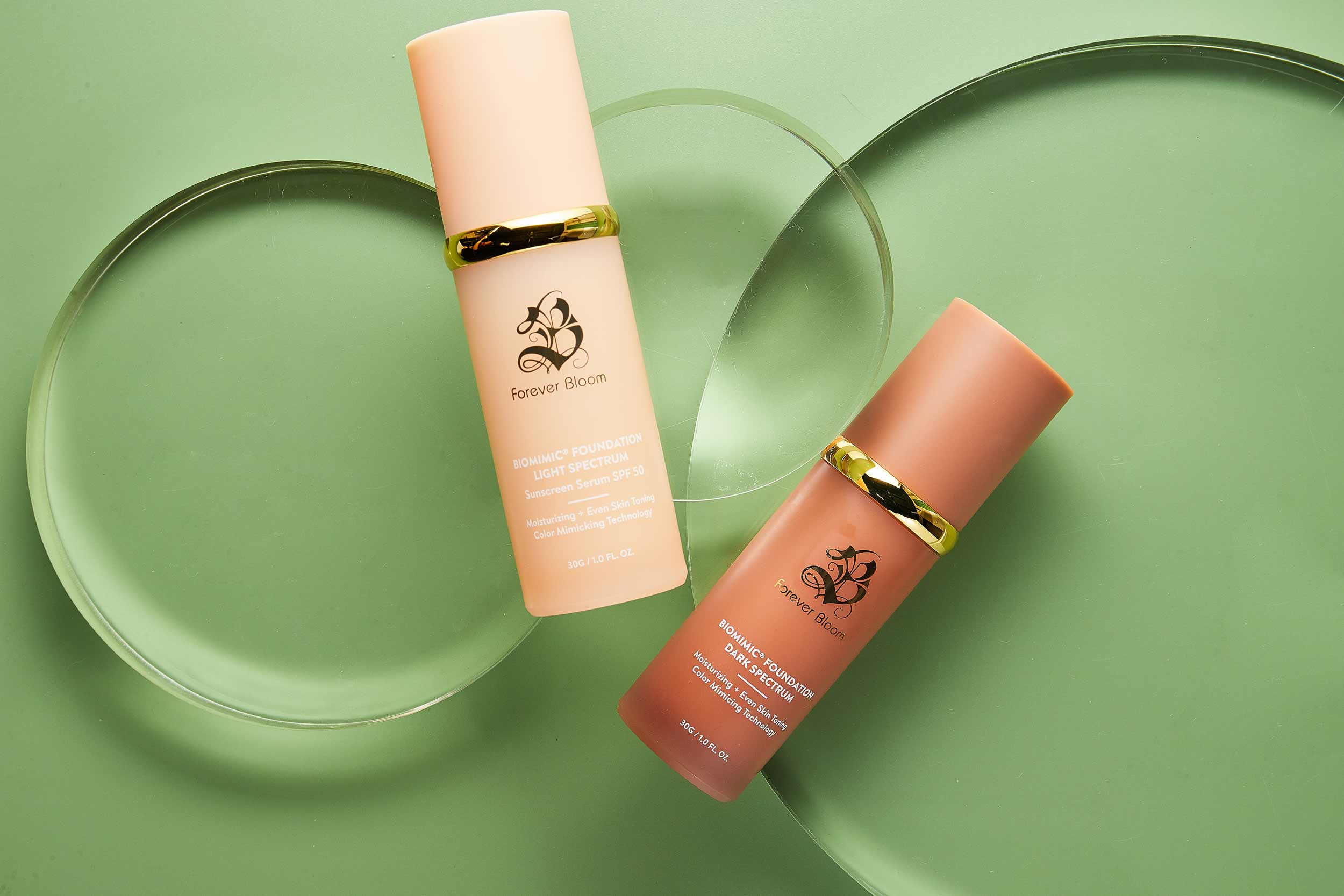 Two biomimic liquid foundation bottles light and dark with gold caps on a green background
