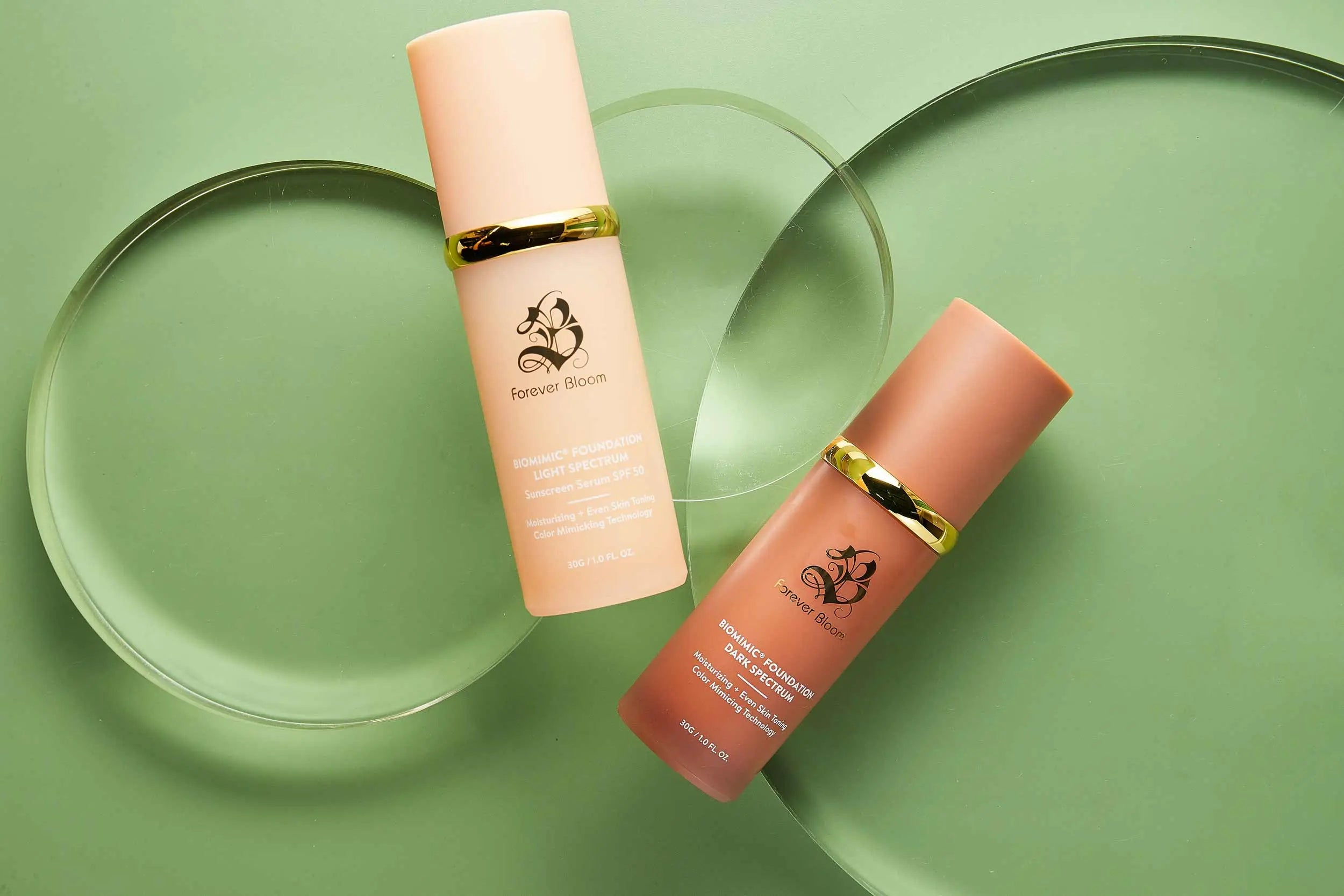 Two biomimic liquid foundation bottles light and dark with gold caps on a green background